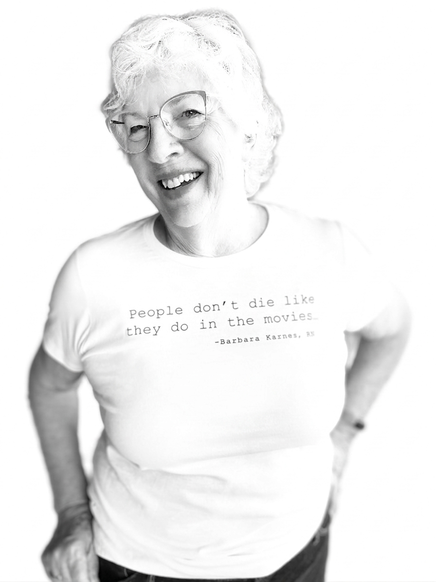 Barbara Karnes, RN wearing a white t-shirt with text that says her quote, People Don't Die Like They Do in the Movies, standing against a white background
