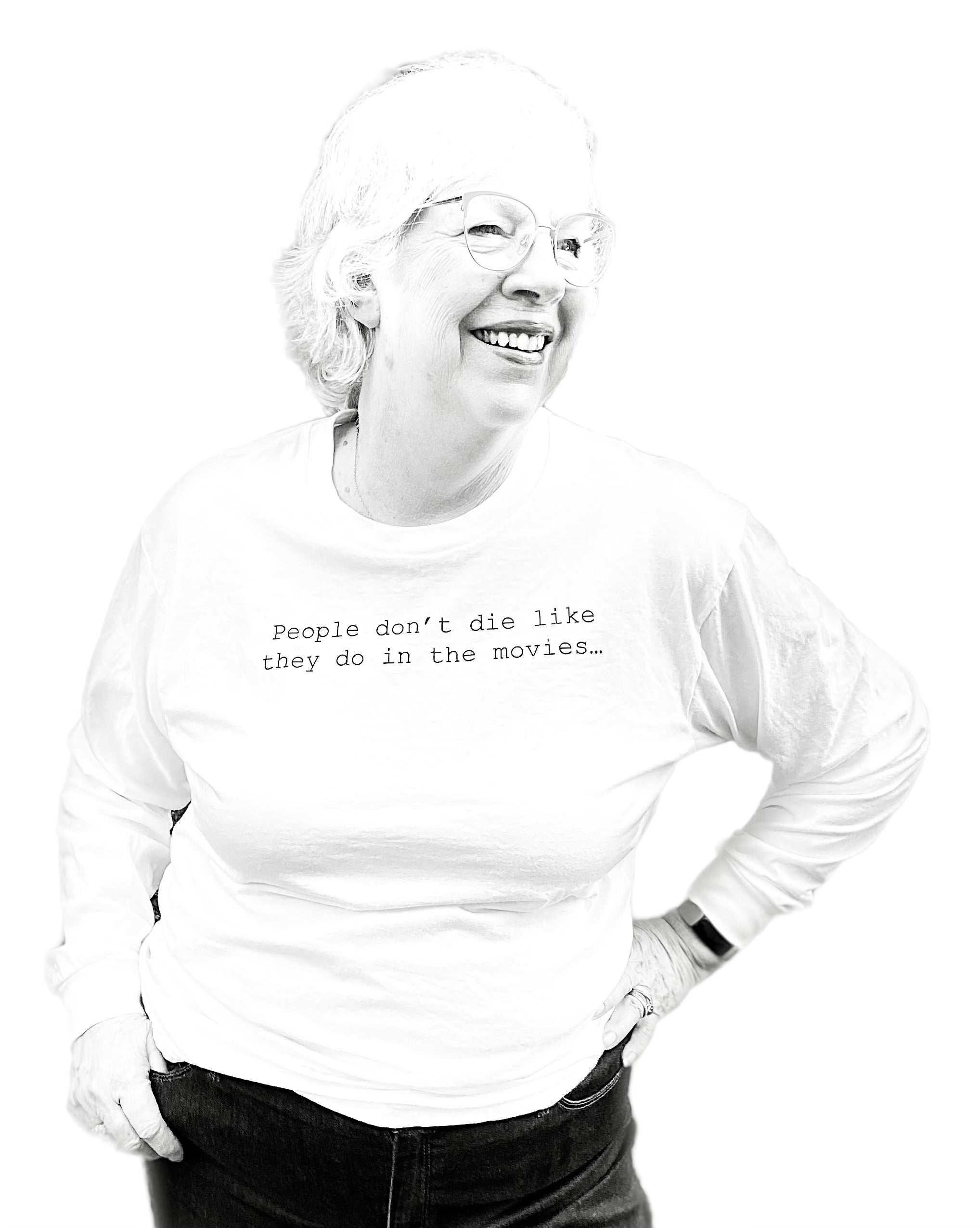 Barbara Karnes, RN wearing a white long sleeve shirt with text that says her quote, People Don't Die Like They Do in the Movies, standing against a white background